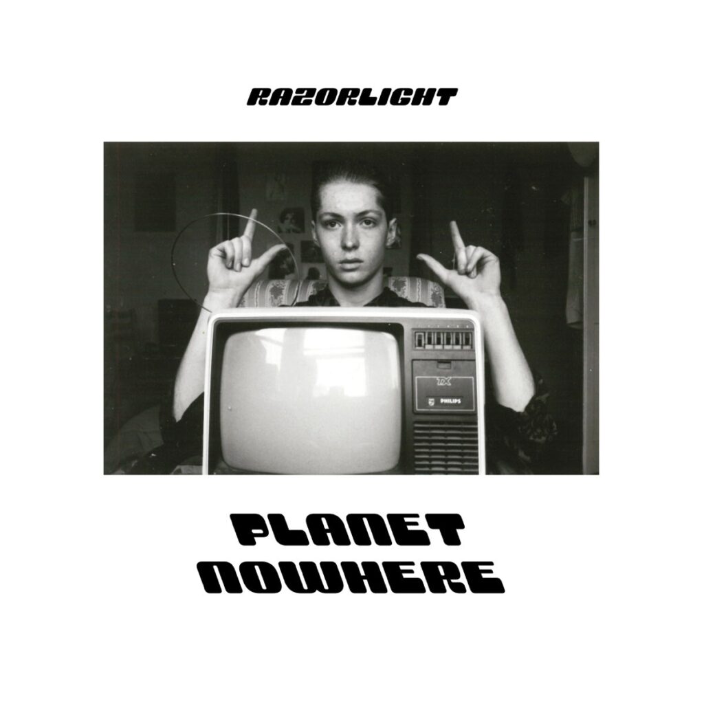 Schwarz-weißes Foto eines Jugendlichen hinter einem alten Fernseher, mit Fingerzeichen wie ein Regisseur – Cover zum Razorlight-Album „Planet Nowhere“.