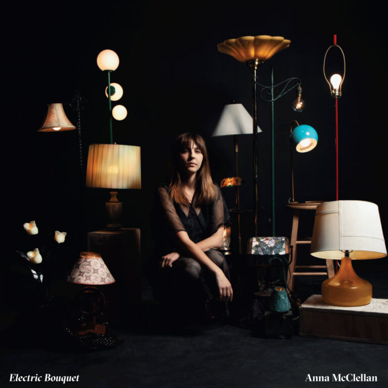 Albumcover von „Electric Bouquet“: Anna McClellan sitzt umgeben von verschiedensten leuchtenden Lampen auf dunklem Hintergrund.