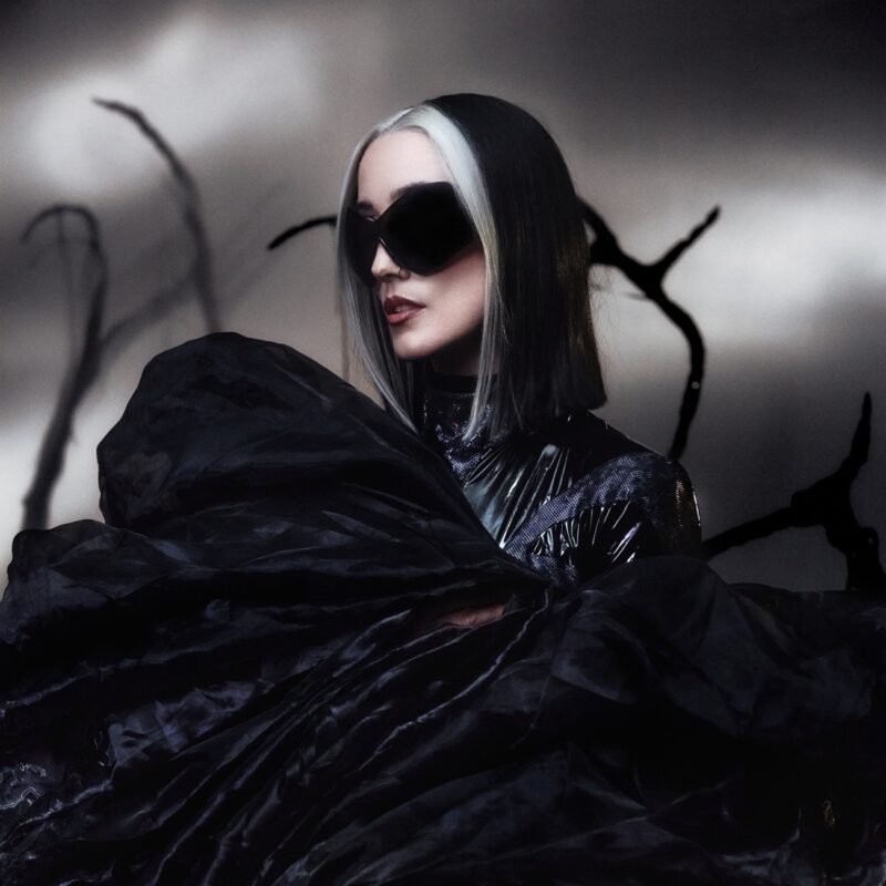 HAYLA in dunkler futuristischer Robe und riesiger Sonnenbrille vor surrealer Kulisse – Artwork des Albums DUSK.