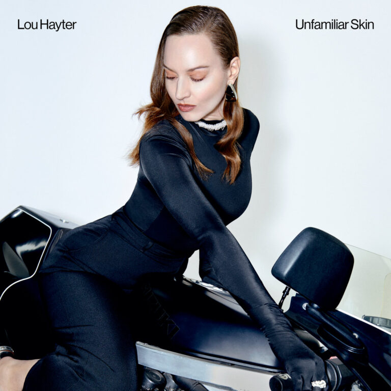 Lou Hayter in eleganter schwarzer Kleidung auf einem Motorrad – Cover zum 80er-inspirierten Electro-Pop-Album „Unfamiliar Skin“.