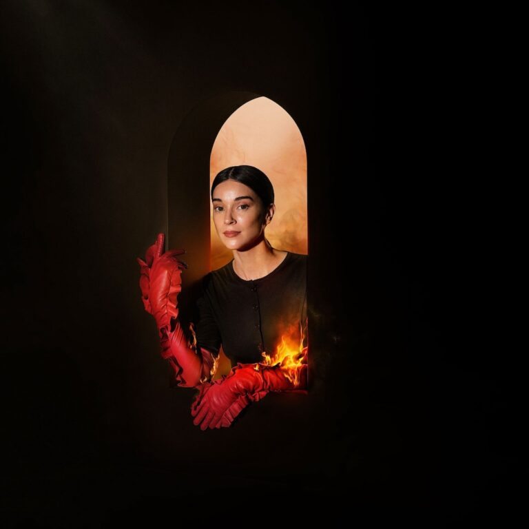 Albumcover mit einer Frau, die in einem dunklen Raum durch ein bogenförmiges Fenster schaut. Sie trägt rote Handschuhe, die in Flammen stehen, vor einem Hintergrund aus orangefarbenem Rauch.