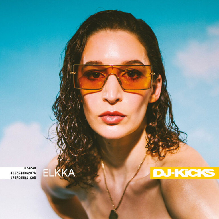 Porträt von Elkka mit orangefarben getönten Sonnenbrillen vor himmelblauem Hintergrund, Cover der DJ-Kicks Compilation mit gelbem Label.