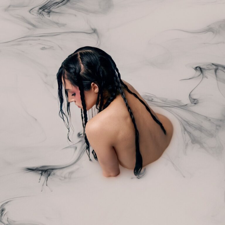 Künstlerin Poppy mit nassen Zöpfen, von oben fotografiert, in milchig-dunklem Wasser – Artwork zum Album Negative Spaces.