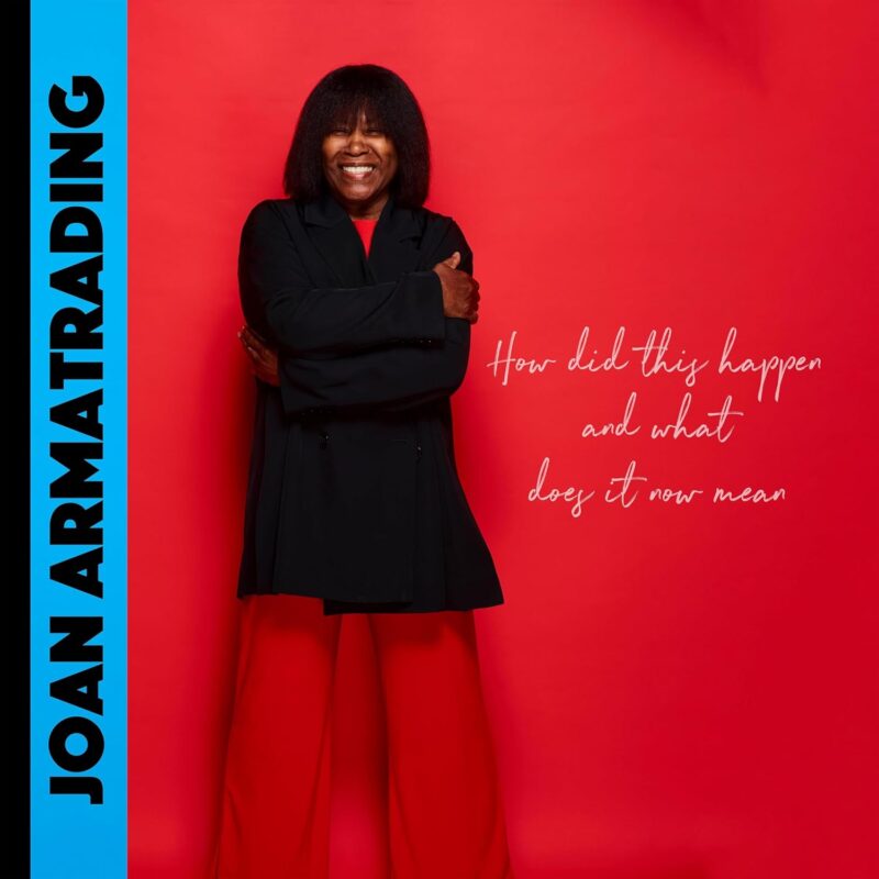Joan Armatrading steht lachend vor rotem Hintergrund, trägt schwarzes Oberteil und rote Hose; links der Albumtitel, rechts der Schriftzug „How did this happen and what does it now mean“.