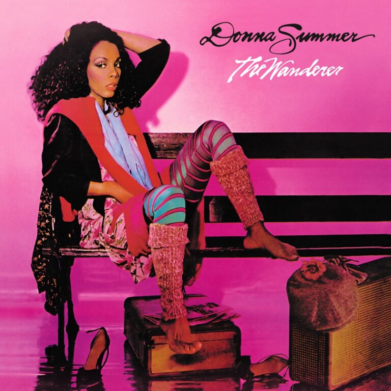 Donna Summer sitzt auf einer Bank, umgeben von Koffern, in einem farbenfrohen Outfit vor pinkem Hintergrund.