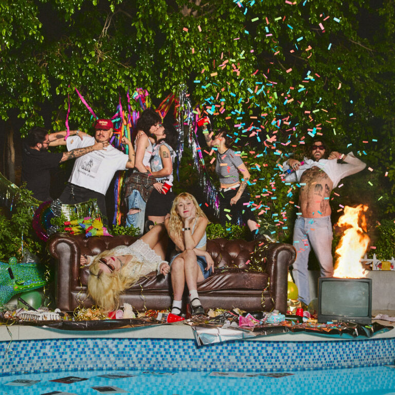 Albumcover von „Who Let the Dogs Out“ der Lambrini Girls: Eine wilde, chaotische Gartenparty mit Sofa, Feuer, Konfetti und queerer Ausgelassenheit am Pool.