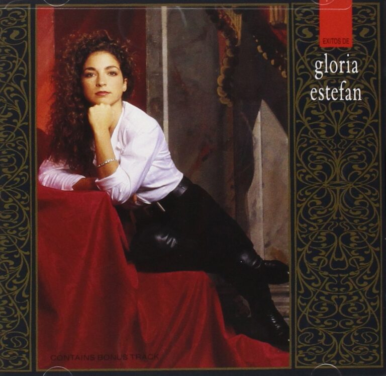 Gloria Estefan posiert in eleganter Kleidung vor einem kunstvollen Hintergrund.