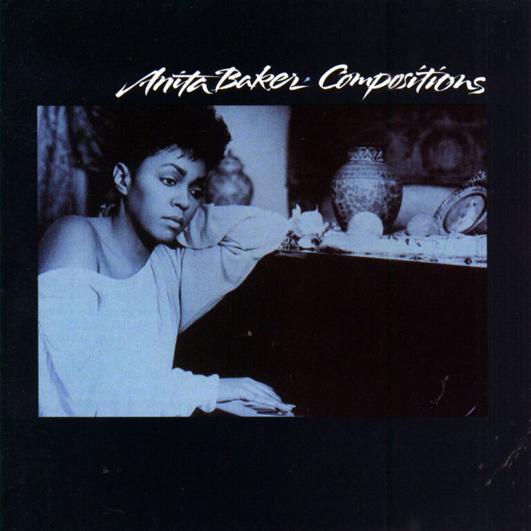 Anita Baker sitzt nachdenklich am Klavier, umgeben von dekorativen Objekten.