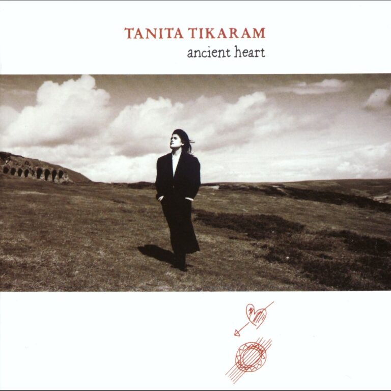 Tanita Tikaram steht auf einer weiten Wiese mit Hügeln im Hintergrund, umgeben von Wolken.