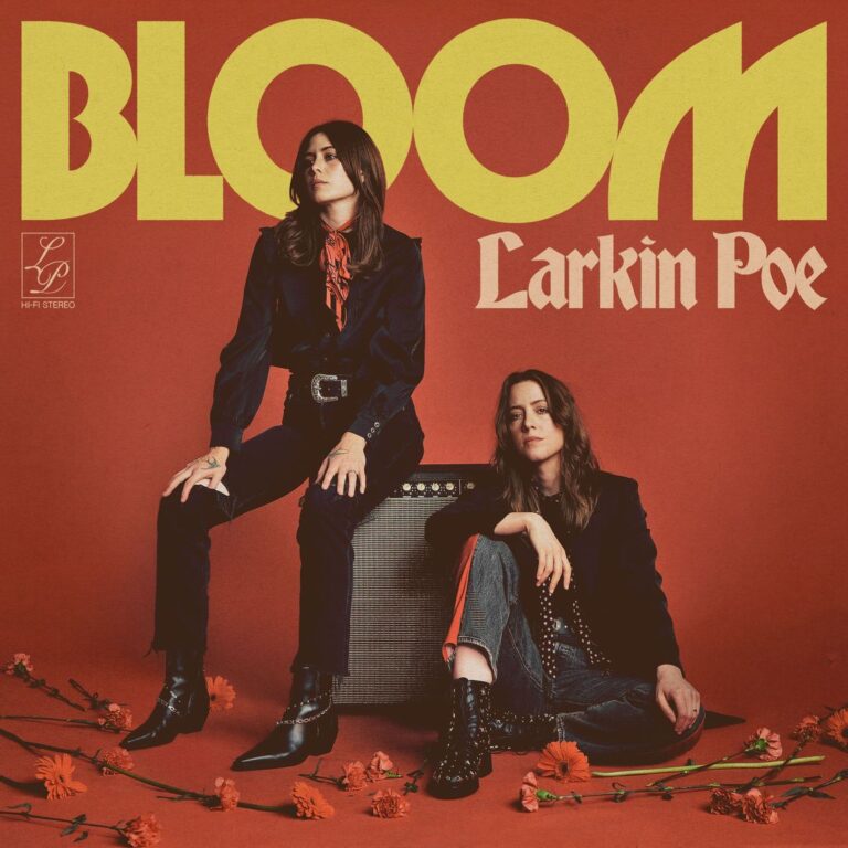 Zwei Musikerinnen in schwarzer Kleidung vor rotem Hintergrund, umgeben von roten Blumen; das Duo Larkin Poe sitzt selbstbewusst vor einem Verstärker – Retro-Look mit moderner Rockattitüde.