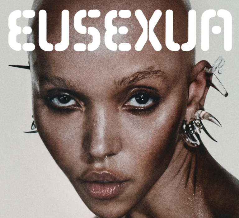 Nahaufnahme eines kahlgeschorenen Gesichts mit intensiven Augen, markantem Schmuck und futuristisch wirkendem Look, darüber der Schriftzug „EUSEXUM“.