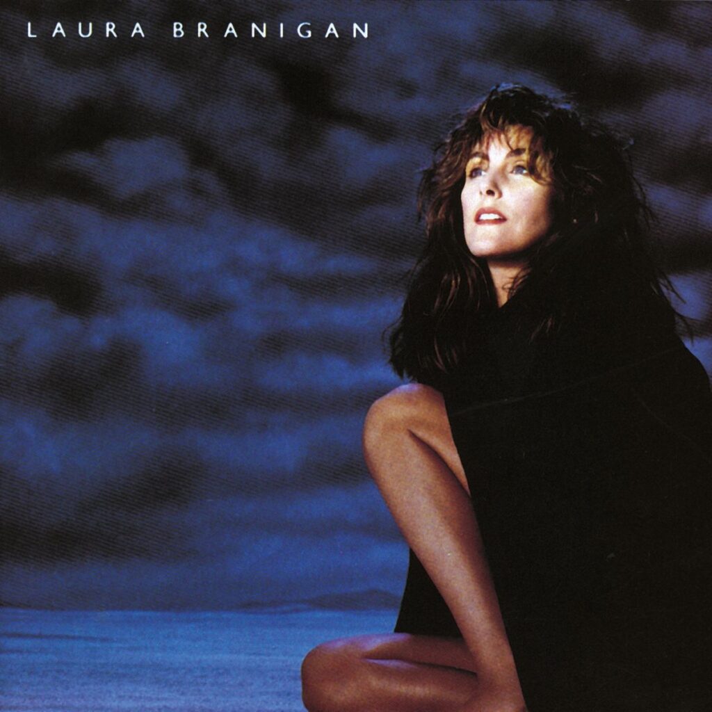Laura Branigan posiert in einem schwarzen Outfit vor einem dramatischen, bewölkten Hintergrund.