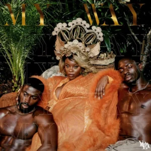 Yola thront in opulentem orangefarbenem Gewand zwischen zwei muskulösen, oberkörperfreien Männern; ein majestätisches, tropisch umrahmtes Cover voller Kraft, Sinnlichkeit und Selbstbestimmung.