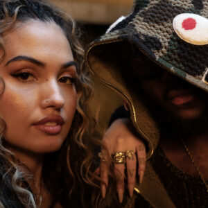 Nahaufnahme von Mabel neben King Promise. Mabels Gesicht ist klar zu sehen, mit glänzendem Make-up und offenen Locken, während King Promise größtenteils unter einer Camouflage-Kapuze verborgen bleibt. Ihre Hände ruhen locker auf seiner Schulter – mit langen Nägeln und auffälligem Schmuck. Die Szene wirkt vertraut, stylish und intensiv – passend zur sinnlichen Stimmung des Songs.