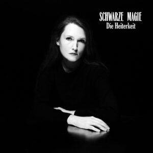 Schwarz-weiß-Porträt von Stella Sommer mit ernstem Blick, Hände auf einem dunklen Tisch – das Cover zu „Schwarze Magie“ strahlt klassische Eleganz und geheimnisvolle Intensität aus.