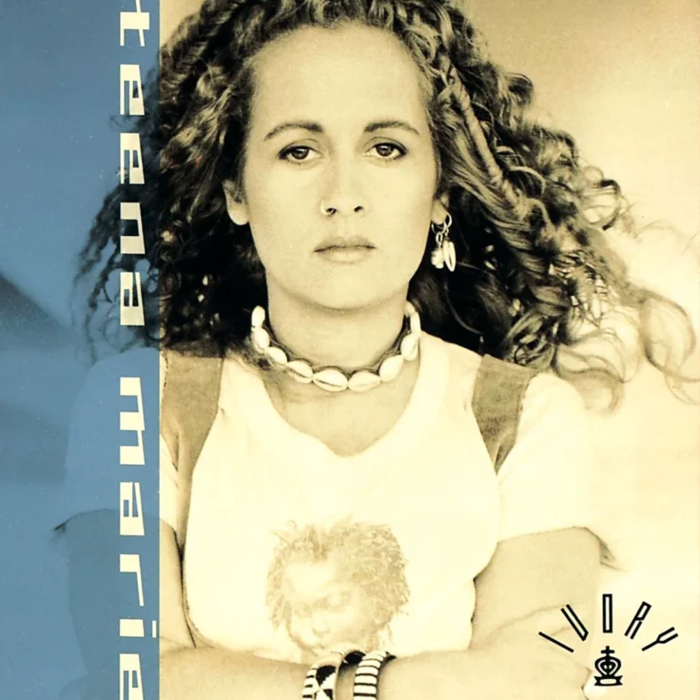 Teena Marie posiert mit lockigem Haar und einem T-Shirt, umgeben von einem blauen Hintergrund.