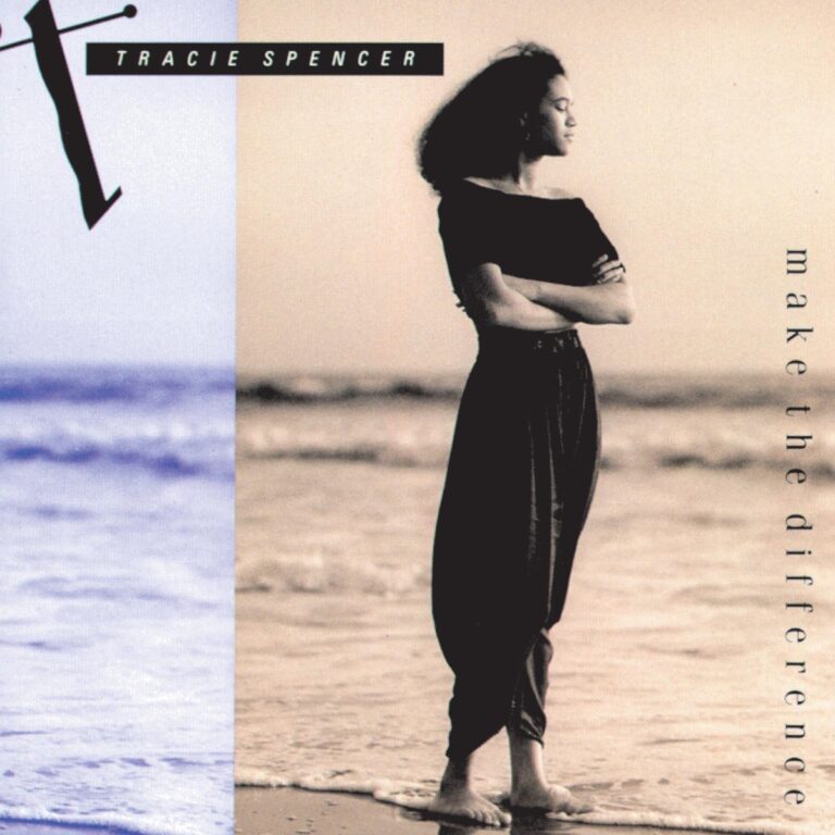 Tracie Spencer steht am Strand in einem schwarzen Oberteil und weiten Hosen, mit Blick auf das Meer.