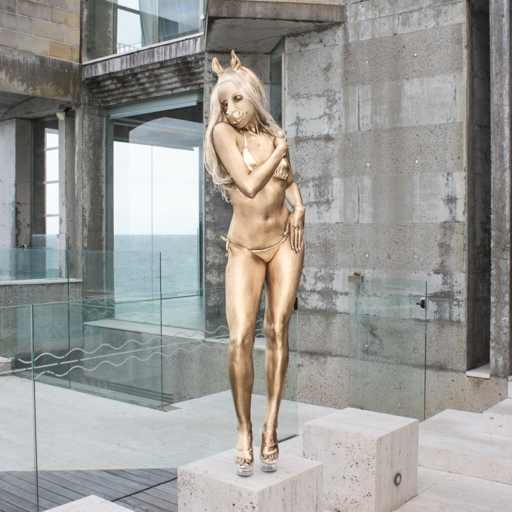 Golden bemalte Person im Bikini und Pferdemaske posiert auf Betonpodest vor moderner Architektur – Cover zur EP „V.I.P.“ von horsegiirL.