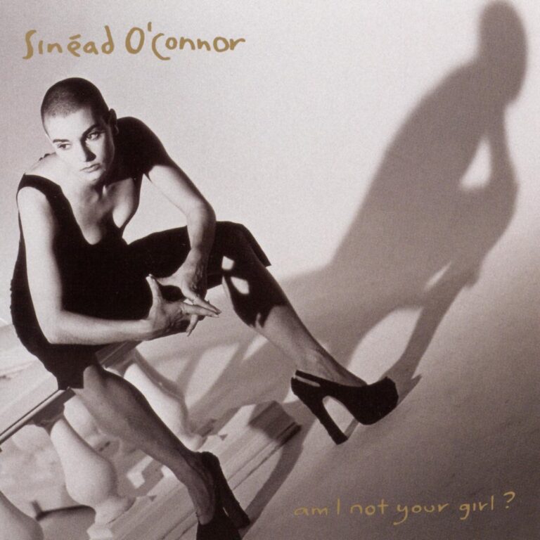 Sinéad OConnor sitzt auf einer Treppe in einem schwarzen Kleid mit Schatten im Hintergrund.