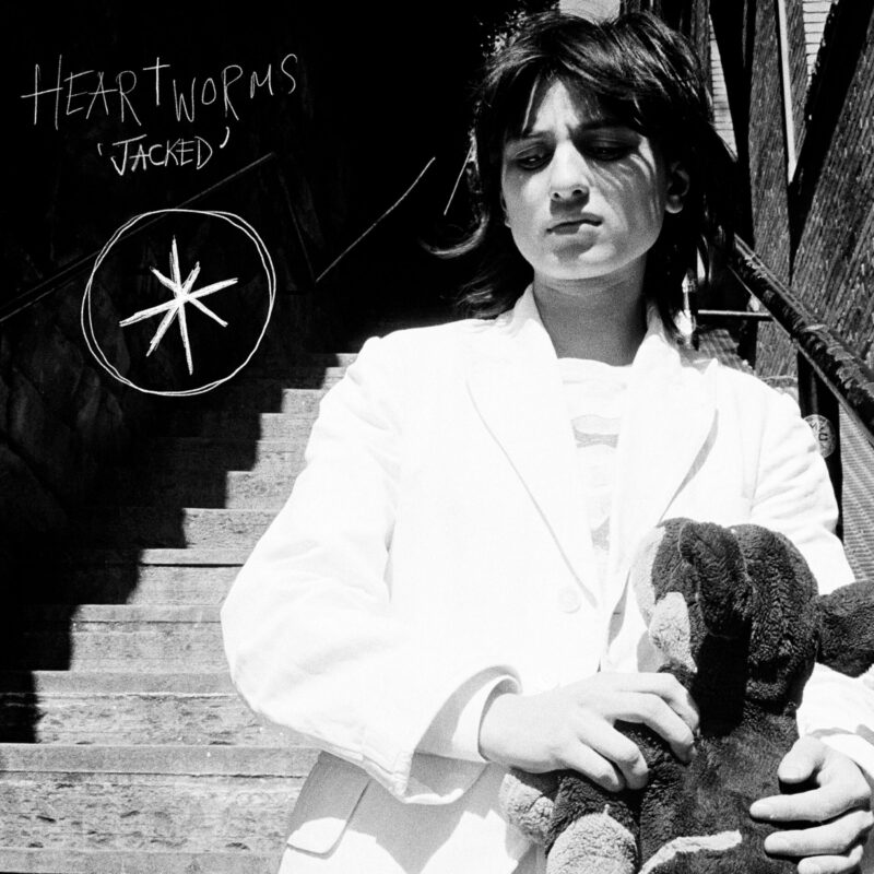 Heartworms in weißem Anzug mit Plüschfigur auf einer Treppe – das kontrastreiche Schwarz-Weiß-Cover zur Single „Jacked“ wirkt roh und verstörend zärtlich.