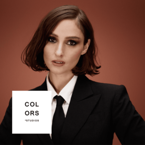 BANKS in schwarzem Anzug und weißem Hemd vor rostfarbenem Hintergrund – ein minimalistisches Portrait, das Stärke, Stil und Ernsthaftigkeit ausstrahlt.