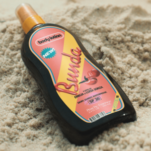 Das Cover zur Single „bunda 🍑“ zeigt ein Sonnenöl-Fläschchen im Sand – ein augenzwinkerndes visuelles Spiel mit dem Songtitel und ein Vorgeschmack auf Sommer, Körperbewusstsein und gute Vibes.