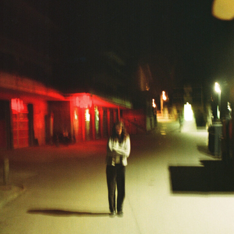 Verwackeltes Nachtfoto einer Person auf leerer Straße, umgeben von rotem Neonlicht – symbolisch für Einsamkeit und emotionale Verlorenheit im Album „Roxwell“.