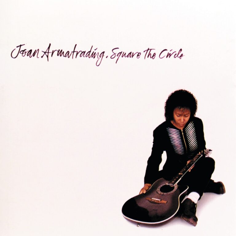 Joan Armatrading sitzt mit einer Gitarre auf weißem Hintergrund.