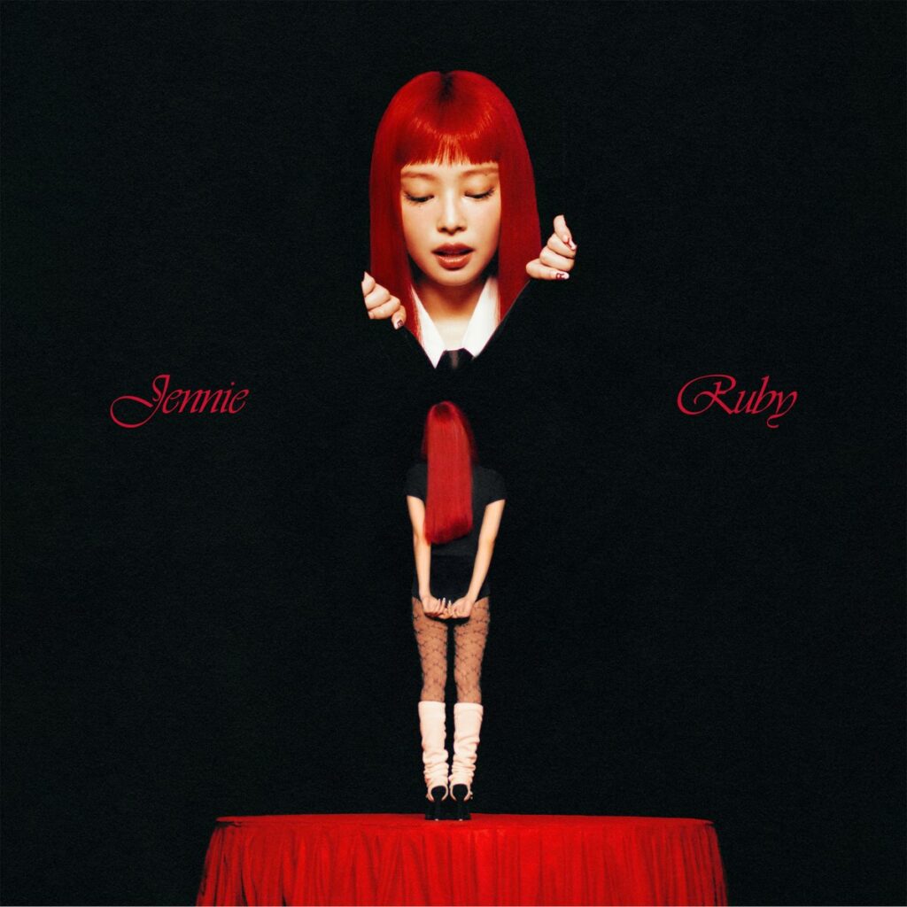 Cover des Albums Ruby von JENNIE: Die Künstlerin mit leuchtend rotem Haar steht auf einem Podest vor schwarzem Hintergrund, eine Miniaturversion ihrer selbst in den Händen haltend.​