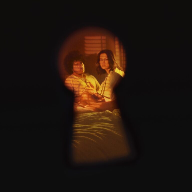 Blick durch ein Schlüsselloch auf zwei Personen in einem Raum, umgeben von warmem Licht und Schatten.