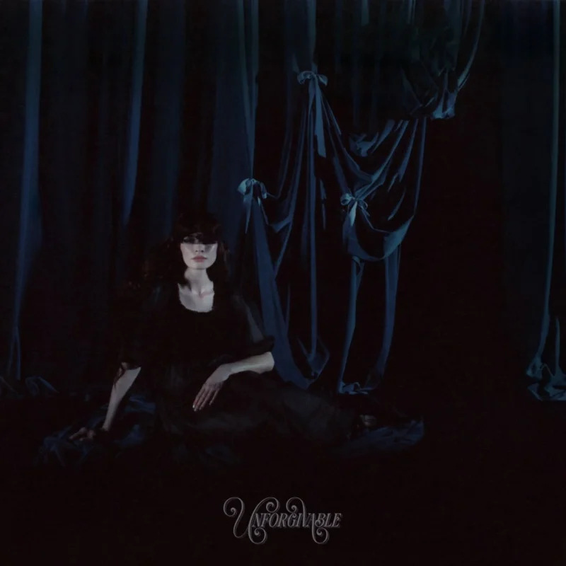 Cover der Single „Unforgivable“ von Alexandra Savior: Die Künstlerin liegt nachdenklich auf einem dunklen Hintergrund mit Lichtpunkten, die eine verträumte Atmosphäre schaffen.​