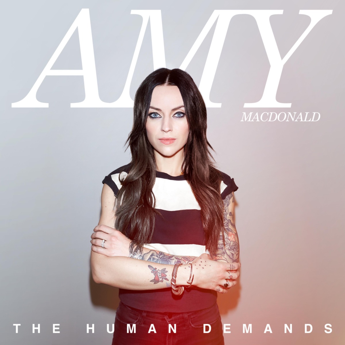 Cover des Albums The Human Demands von Amy Macdonald: Die Künstlerin steht mit verschränkten Armen vor neutralem Hintergrund, ernst und introspektiv.