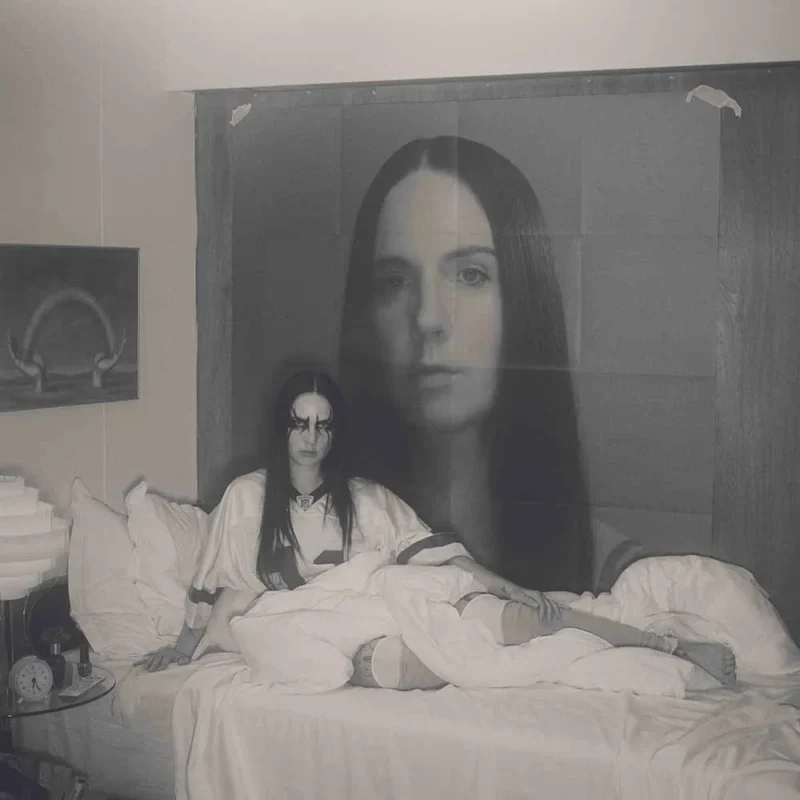 MØ sitzt in einem weißen Bett unter einem riesigen Porträt von sich selbst – Albumcover von „Plæygirl“