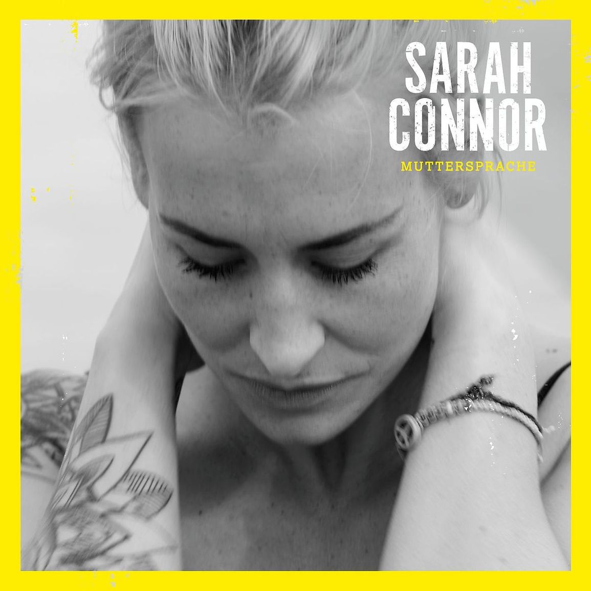 Schwarzweißporträt von Sarah Connor mit gesenktem Blick und Tattoo, eingerahmt von einem leuchtenden Gelb