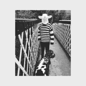 Kathryn Joseph im Schafskostüm mit Hund im Skelettmantel auf Brücke – surreal und symbolisch für das Album „WE WERE MADE PREY.“