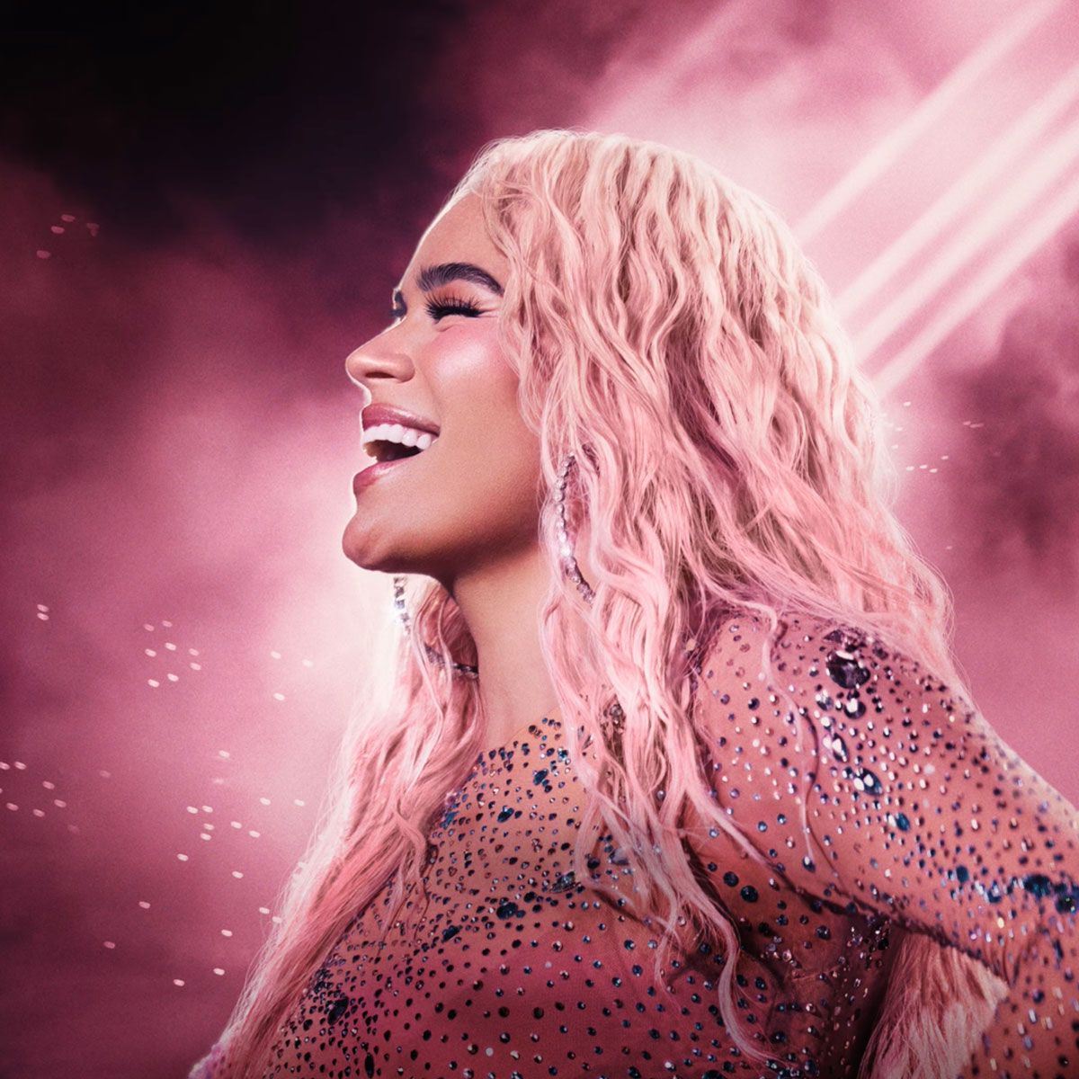 Karol G mit pastellrosa Haaren im Profil, lächelnd vor einem nebelig-rosa Hintergrund – das offizielle Artwork zur Single „Milagros“, das eine sanfte und introspektive Atmosphäre ausstrahlt.