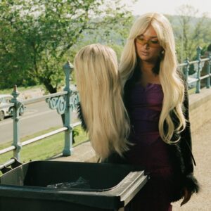 Joy Crookes mit blonder Perücke in der Hand – Szene aus dem Carmen-Video als Sinnbild für abgelegte Schönheitsnormen.
