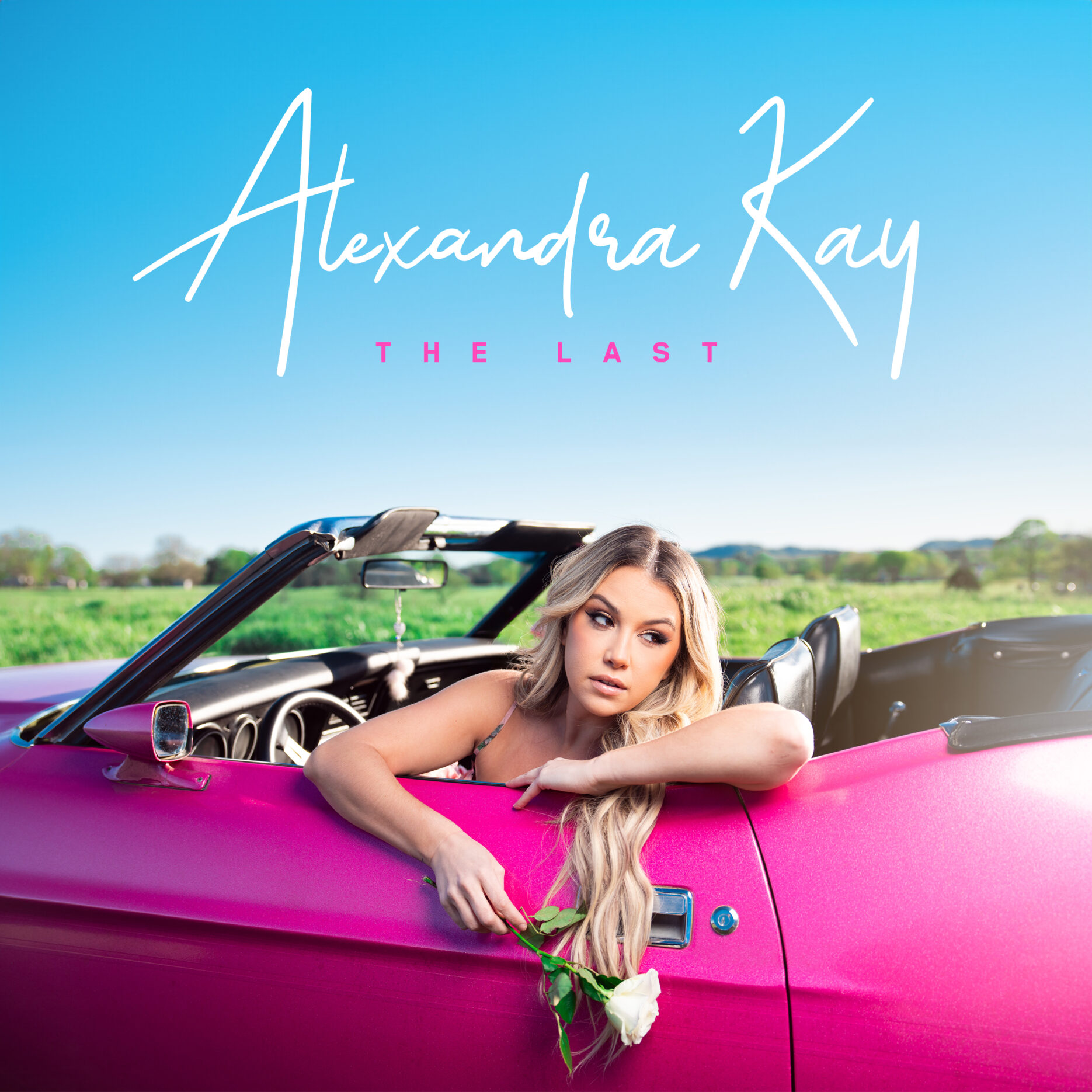 Alexandra Kay lehnt im pinken Cabrio mit weißer Rose in der Hand vor blauem Himmel.