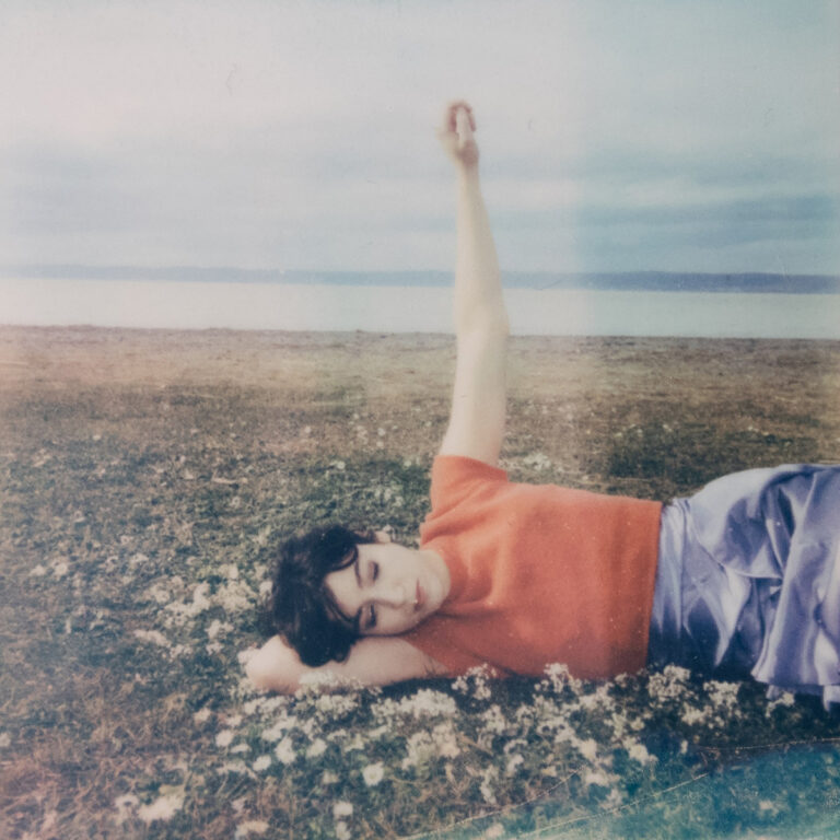Das Albumcover von OSKA – Refined Believer zeigt eine junge Frau im Gras liegend mit erhobenem Arm, träumerisch und zart inszeniert.