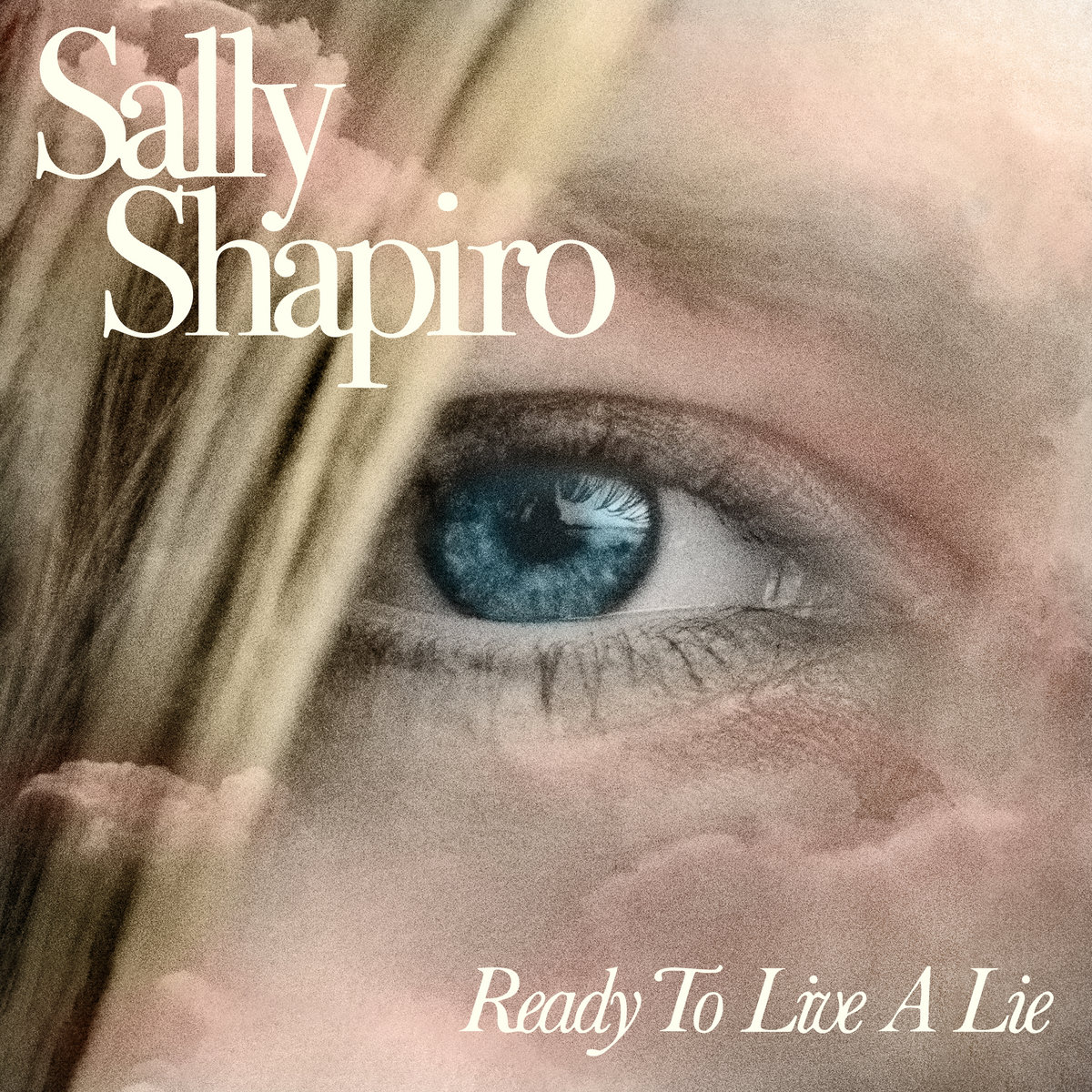 Nahaufnahme eines blauen Auges im Nebel, Albumcover von Sally Shapiros Ready to Live a Lie mit zartem Schriftzug vor pastellfarbenen Wolken.