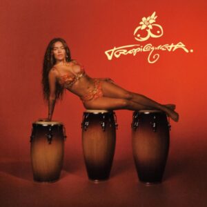 Karol G posiert im Glitzeroutfit auf drei Congas vor rotem Hintergrund – das Albumcover von „Tropicoqueta“ versprüht Showgirl-Glamour und Latin-Energie.
