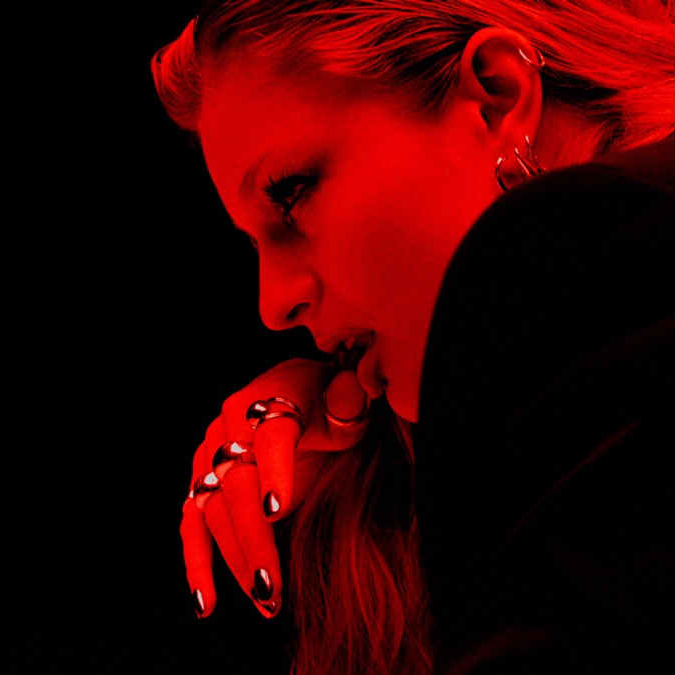 Rotes Porträt von Dylan mit dramatischem Licht, im Profil mit ernster Miene und silbernen Ringen