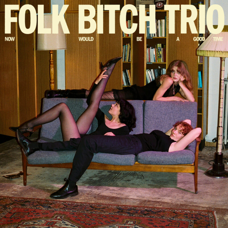 Albumcover Now Would Be A Good Time von Folk Bitch Trio mit drei Musikerinnen auf einem Sofa in warmer, retrohafter Wohnzimmerstimmung.