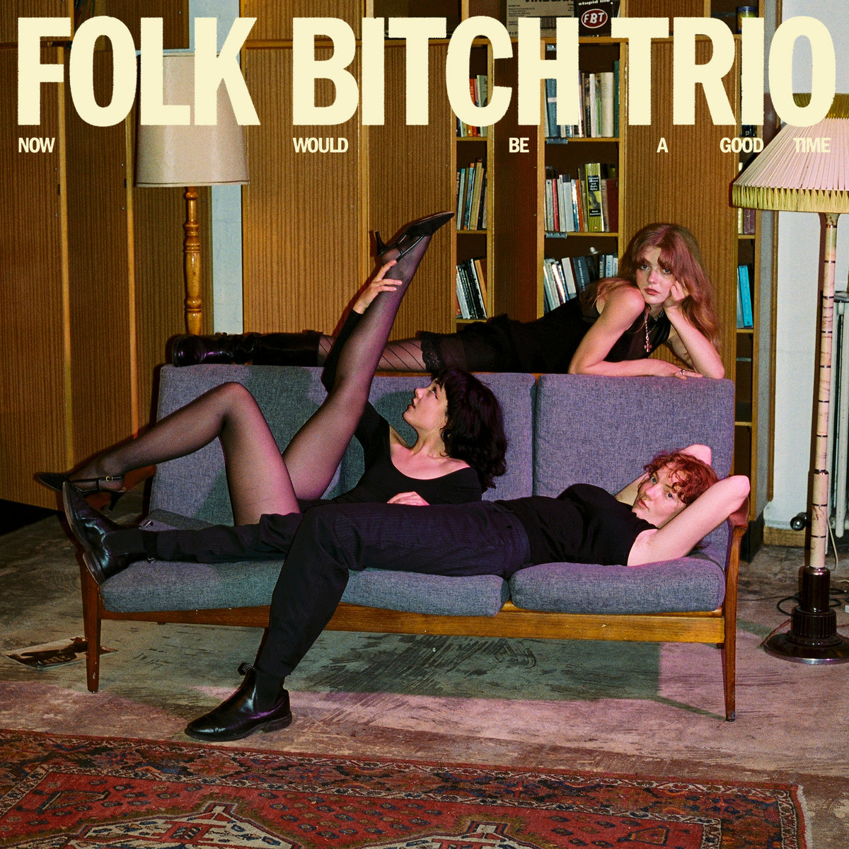Albumcover Now Would Be A Good Time von Folk Bitch Trio mit drei Musikerinnen auf einem Sofa in warmer, retrohafter Wohnzimmerstimmung.