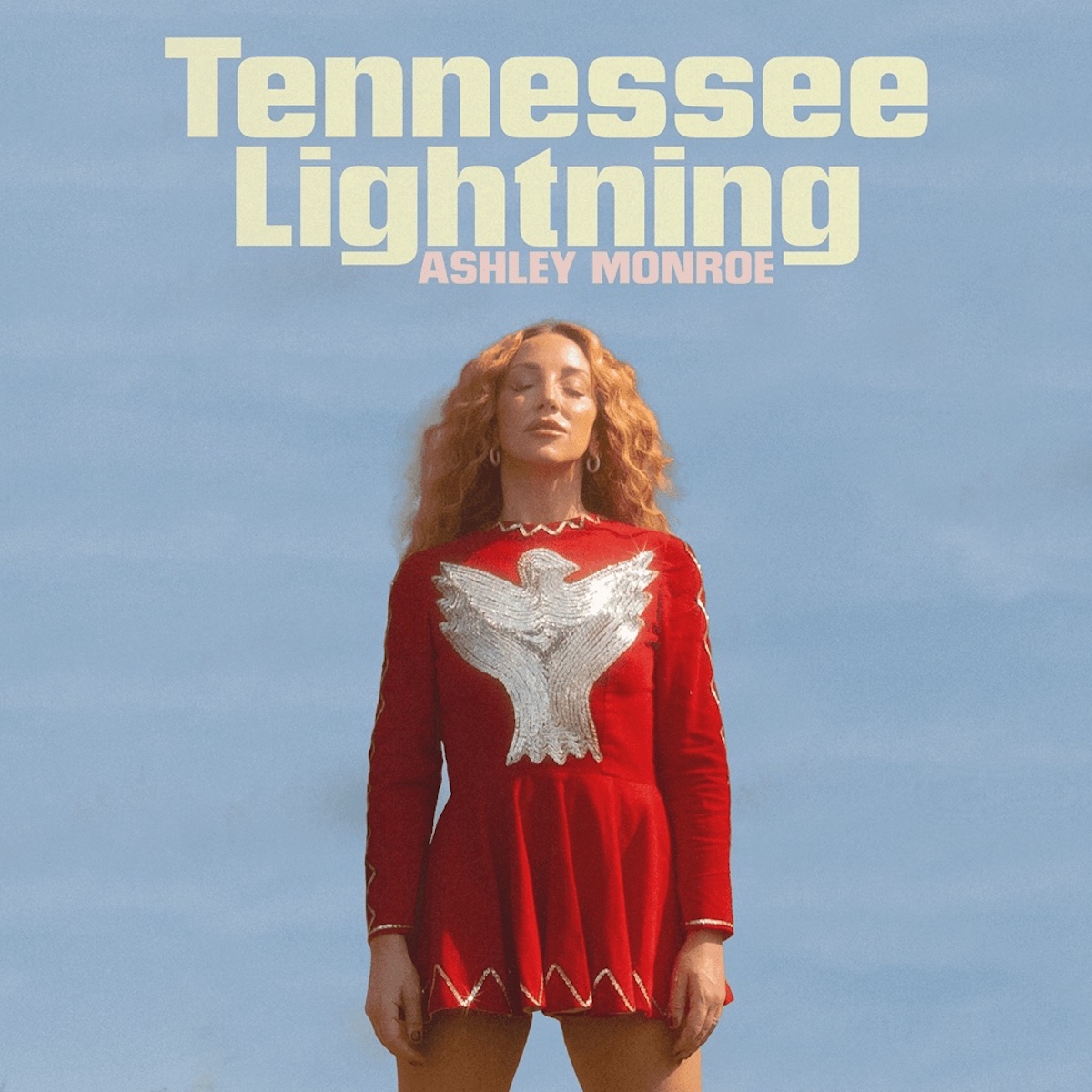 Ashley Monroe im roten Kleid mit silberner Taube vor blauem Himmel – Cover des Albums „Tennessee Lightning“