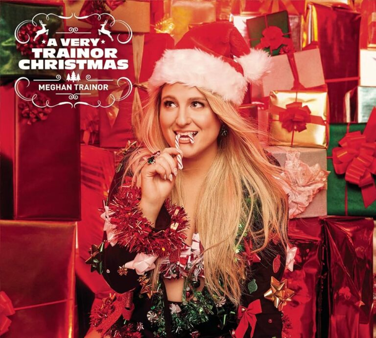 Meghan Trainor mit Santa-Mütze vor roten Geschenken, hält eine Zuckerstange, glitzerndes Tinselkleid in einer festlich roten Kulisse.