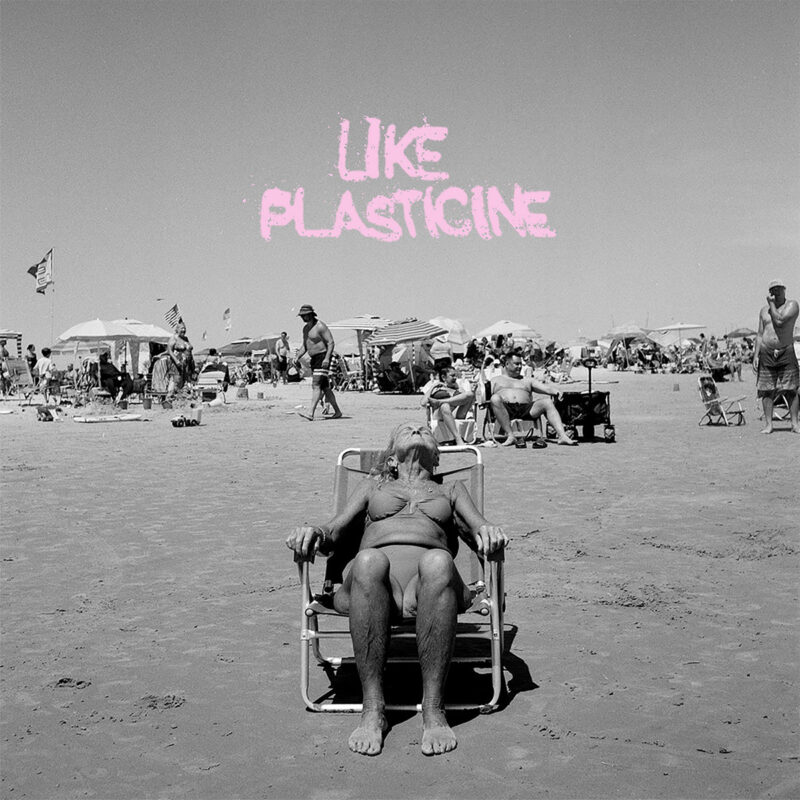 Schwarzweißfoto einer älteren Frau im Bikini auf einem Strandstuhl, im Hintergrund eine belebte Strandkulisse, darüber rosa Schrift „Like Plasticine“.