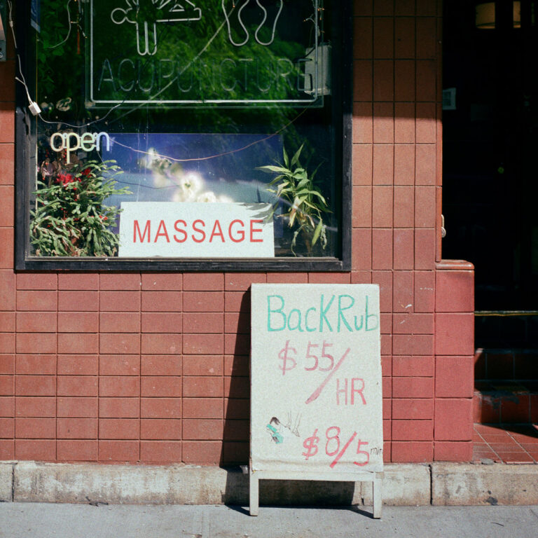 Albumcover zeigt ein Straßenschild vor einem Massage-Studio mit handgeschriebener Preisangabe.