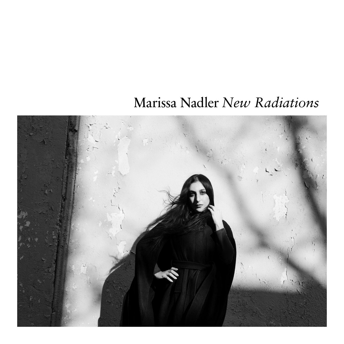 Schwarzweiß-Cover von New Radiations: Marissa Nadler lehnt an einer Wand, im Schattenwurf, im langen dunklen Kleid.