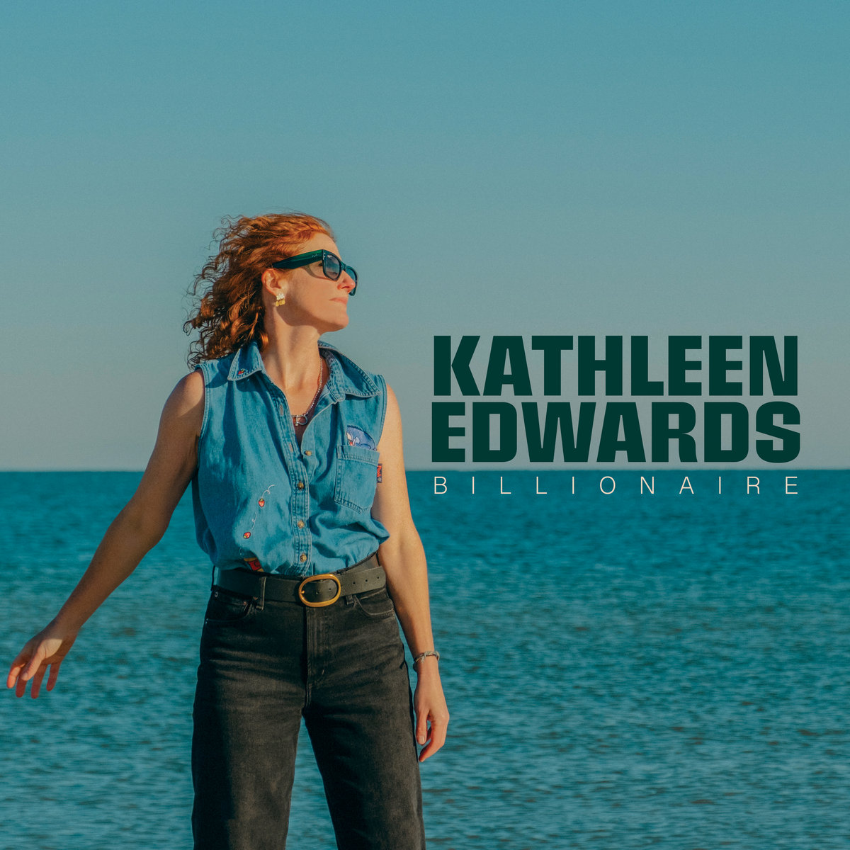 Albumcover von Kathleen Edwards – „Billionaire“: Die Künstlerin steht im Jeanshemd am Meer, mit Sonnenbrille, Blick ins Licht, klare Schriftzüge daneben.
